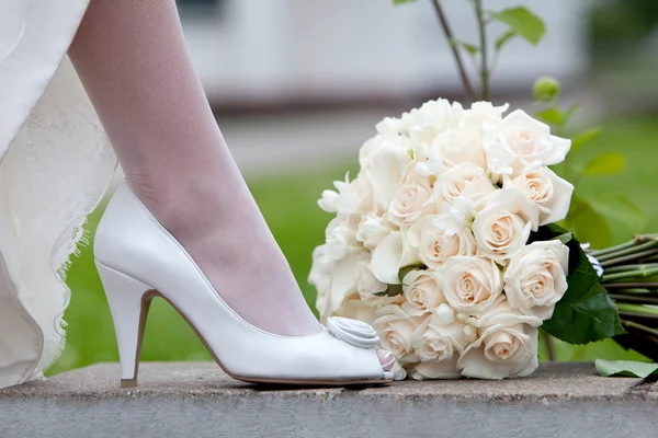 婚礼鞋和新娘花束。女性的脚，穿着白色的婚纱的鞋子和花束的新鲜的白玫瑰特写. — 图库照片