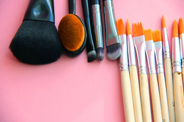 makeup brushes and paint brushes on a light background