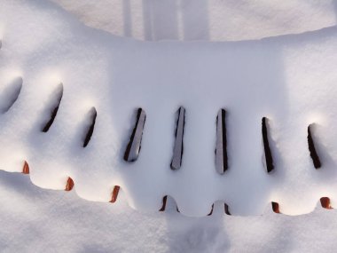 Şehir parkında kar kaplı bank, kış manzarası.