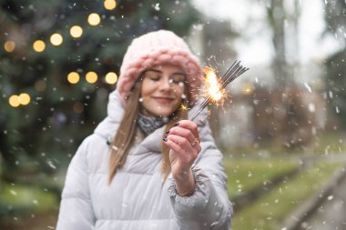 Gülümseyen bir kadın yeni yıl ağacının yanında maytaplarla eğleniyor.