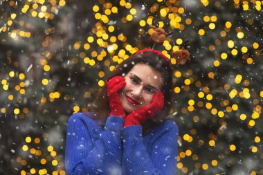 Güzel esmer kadın, kar yağarken Noel panayırında yürüyen komik saç halkası ve kırmızı eldivenler takıyor.