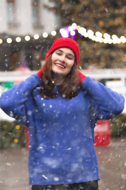 Güzel esmer kadın, kar yağarken Noel panayırında yürüyor.