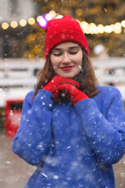 Mutlu esmer kadın, kar yağarken Noel panayırında yürüyor.