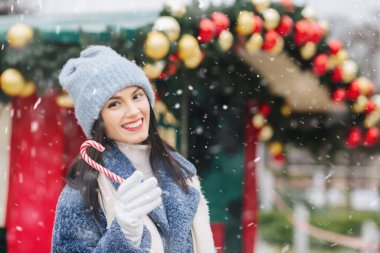 Neşeli esmer kadın kar yağarken örgü şapka ve kışlık palto giyiyor. Metin için boşluk