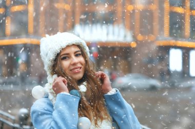 Muhteşem esmer kadın, kar yağarken şehirde çelenklerle süslenmiş örgü şapka ve palto giyer. Metin için boşluk