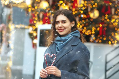 Neşeli esmer kadın kar yağarken kalp şeklinde şeker tutuyor.