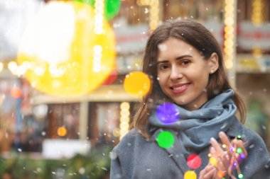 Neşeli kadın kar yağışı sırasında bokeh ışığıyla sokakta yürürken gri bir ceket giyiyor. Boş boşluk