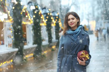 Güzel esmer kadın, kar yağarken Noel panayırının yanında hediye kutusu tutuyor. Metin için boşluk