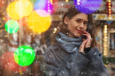 Güzel bir kadın kar yağışı sırasında sokakta elinde bokeh ışığıyla yürürken gri bir ceket giyer. Boş boşluk