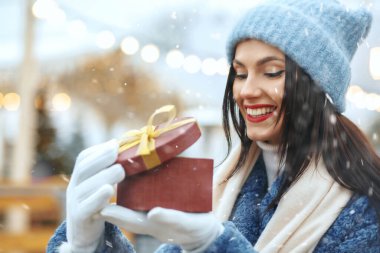 Kar yağışı sırasında elinde hediye kutusu tutan kışlık paltolu, mutlu esmer kadın. Metin için boşluk