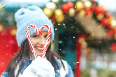 Neşeli esmer kadın, kar yağarken kalp şeklinde şeker tutuyor. Metin için boşluk