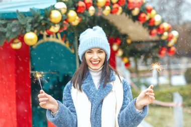 Zarif genç bayan mavi ceket giyiyor kar yağarken Bengal ışıklarıyla tatilin tadını çıkarıyor