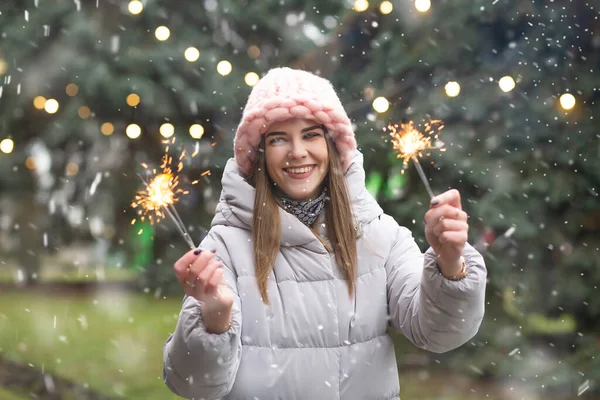 下雪天 一个兴奋的微笑的女人在圣诞树旁与火花嬉戏 — 图库照片