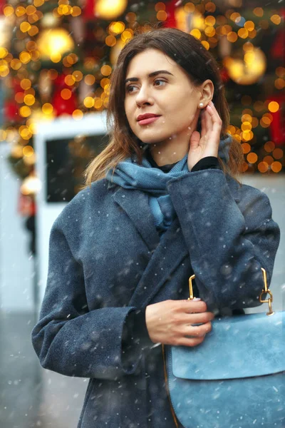 Güzel, genç bir bayan, kar yağarken sokakta yürürken şık bir palto giyer.