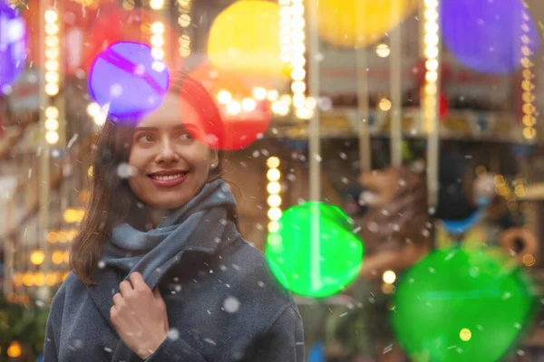 Neşeli kadın kar yağışı sırasında bokeh ışığıyla sokakta yürürken gri bir ceket giyiyor. Boş boşluk