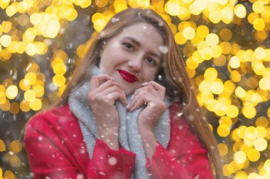 Kar yağışı sırasında sokak fuarında yürüyen kırmızı paltolu hoş bir genç kadın.