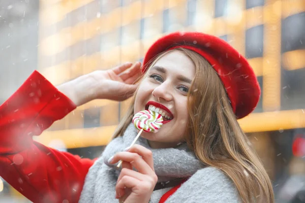 Ładna Młoda Kobieta Czerwonym Płaszczu Gryzie Słodycze Podczas Opadów Śniegu — Zdjęcie stockowe