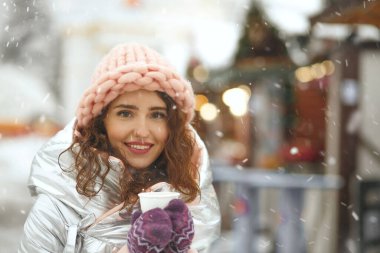 Kar yağışı sırasında kış fuarında kahve içen çarpıcı genç bir kadın. Boş boşluk