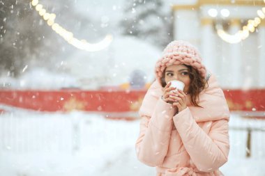 Güzel genç bayan kar yağışında kış festivalinde sıcak şarap içiyor. Boş boşluk