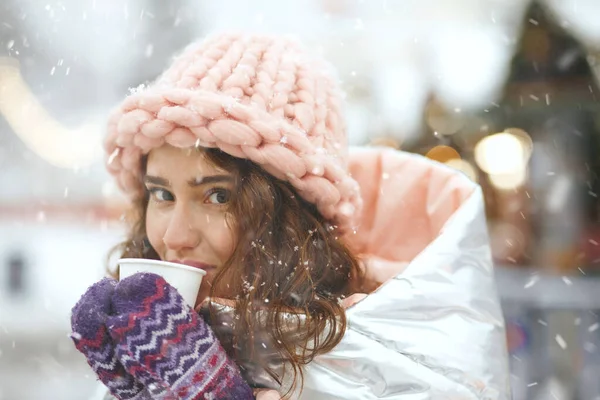 Kar yağışı sırasında kış fuarında sıcak şarap içen muhteşem genç kadın. Boş boşluk