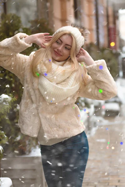 雪の中 色とりどりのガーランドの近くの街を歩く素敵なブロンドの女性 — ストック写真