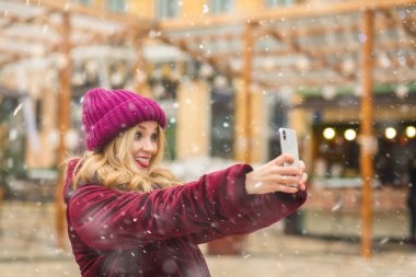 Havalı genç bir kadın kış pazarında selfie çekiyor.