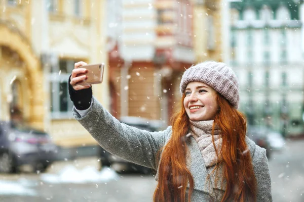 Iloinen Inkivääri Nainen Pitkät Hiukset Ottaen Selfie Matkapuhelimeensa Lumisateen Aikana — kuvapankkivalokuva