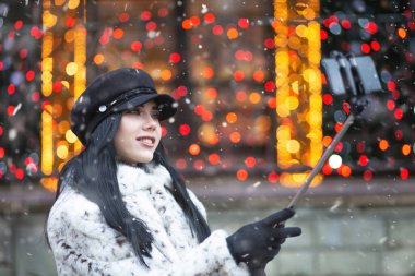 Şık, esmer, uzun saçlı bir kadın Noel fuarında akıllı telefonuyla selfie çekiyor. Metin için boşluk