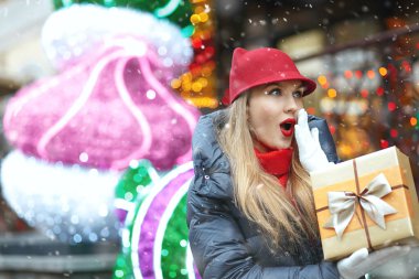 Kar yağarken sokakta elinde hediye kutusu olan heyecanlı sarışın bir kadın. Boş boşluk