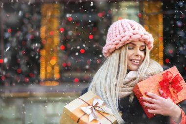 Gülümseyen sarışın kadın kış fuarında örülmüş pembe şapka takıyor ve hediyelerin tadını çıkarıyor. Metin için boşluk