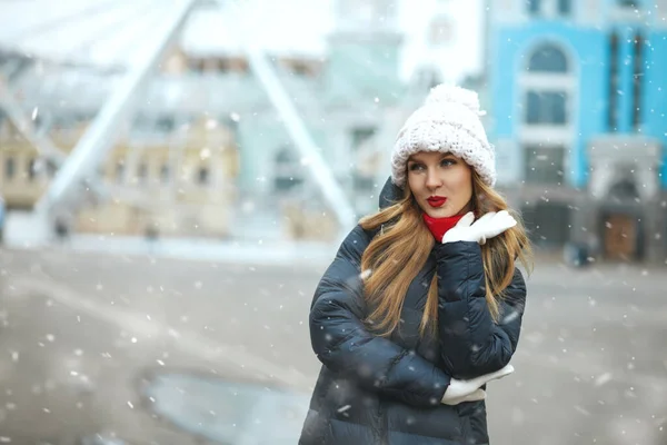 飘飘欲仙的金发女子头戴针织的帽子 在降雪时步行在城市里 案文的篇幅 — 图库照片