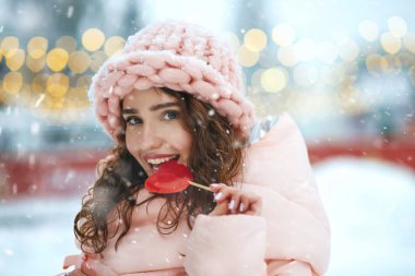 Flirty esmer kadın pembe şapka, kalp şeklinde tatlı kırmızı şeker ısırıyor. Metin için boşluk