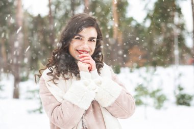 Neşeli kıvırcık esmer kadın kar yağarken ormanda yürürken kalın bir palto giyer. Boş boşluk