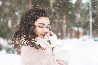 Zarif kıvırcık esmer kadın kar yağışı sırasında ormanda yürürken kalın bir palto giyer. Boş boşluk