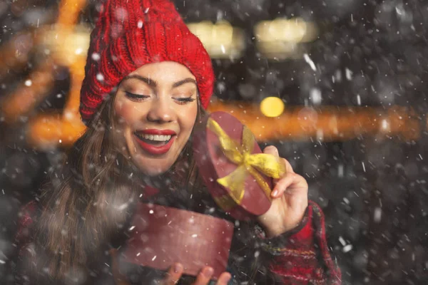 Surprised young woman receiving a gift at the Christmas market during snowfall. Space for text