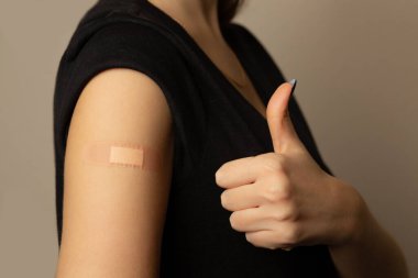 Aşıyı aldıktan sonra kolunda yapıştırıcı olan kadın baş parmağıyla işaret veriyor.