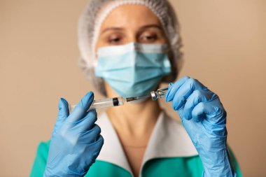 Kadın doktor, hastanede maske takıyor ve şırıngayı kovid 19 aşısıyla dolduruyor.