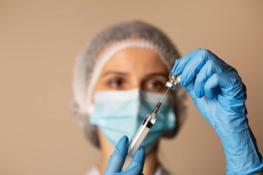 Maskeli kadın doktor hastanede Coronavirus aşısıyla şırınga dolduruyor.