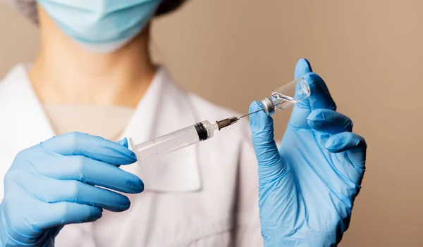मेडिकल पोशाक और लेटेक्स दस्ताने में महिला डॉक्टर इंजेक्शन के लिए तैयार वैक्सीन के साथ सिरिंज भर रहा है — स्टॉक फ़ोटो, इमेज
