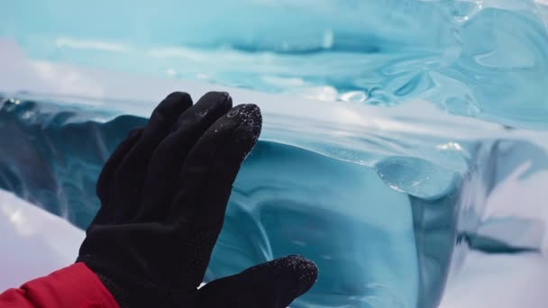 Uomo in guanti neri e giacca rossa toccando la superficie del blocco di ghiaccio turchese lucido — Video Stock