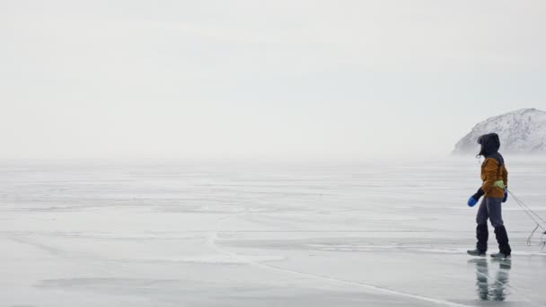 Людина з обладнаними санчатами рухається через заморожений лід. Сніговий туманний сірий пейзаж — стокове відео