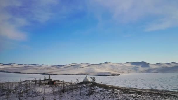 Luchtfoto 's. Witte boeddhistische stoepa op de top van besneeuwde heuvel. Bevroren ijsmeer rond — Stockvideo