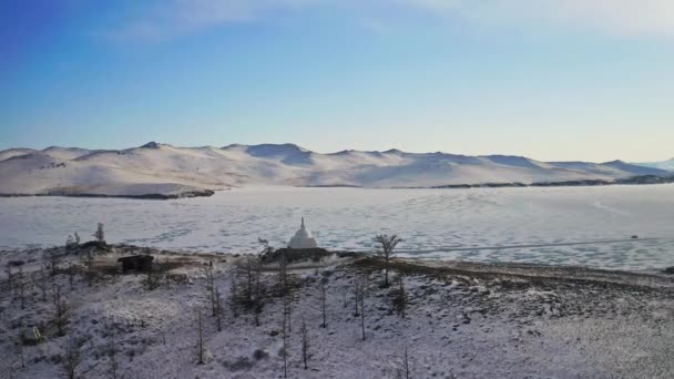 Воздушная панорама. Белая буддийская ступа на вершине снежного холма возле ледяного озера — стоковое видео