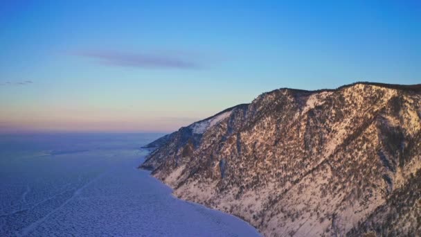 Vista aérea de pájaro. Montaña nevada a la hora dorada redondeada con lago helado — Vídeos de Stock