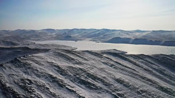 Panorama zimy lotniczej. Zamarznięte jezioro pokryte lodem. Śnieżne wzgórza w słońcu. — Wideo stockowe
