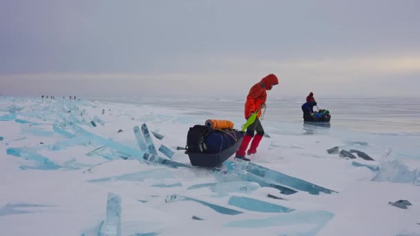 Touriste en tenue d'hiver rouge avec luge surmonter barrière de glace enneigée sur son chemin — Video