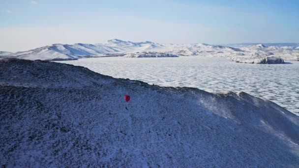 O paraglide vermelho sobe para o ar. Voe acima da colina de neve. Aterragem no lago de gelo congelado — Vídeo de Stock