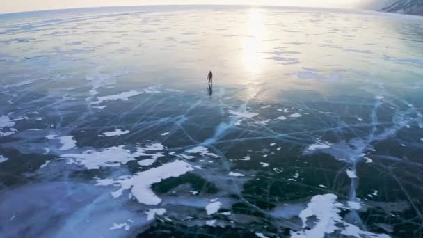 Widok z lotu ptaka. Samotny człowiek jeździ po zamarzniętym jeziorze. Zjeżdżalnie na gładkim ciemnym popękanym lodzie — Wideo stockowe