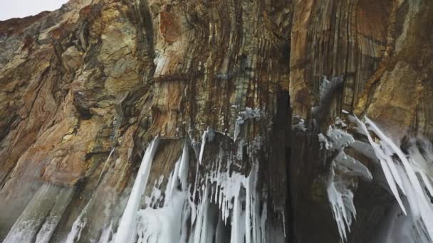 Ice grotto in huge brown rock, stalactites, white frozen icicles hang on ceiling — Stockvideo