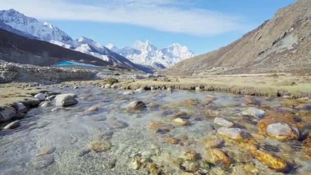 Fresco río de tierras altas poco profundas fluye sobre piedras grises húmedas cerca de picos nevados — Vídeo de stock